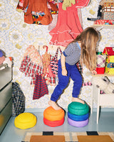 Child playing with colorful Stapelstein Rainbow in a room with toys and clothing on the wall.