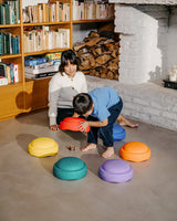 Woman and child playing with colorful Stapelstein rainbow set in a cozy room with a fireplace and bookshelf.