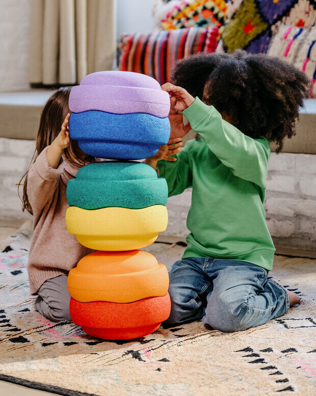 Two children playing with a colorful stack of toys on a patterned rug.