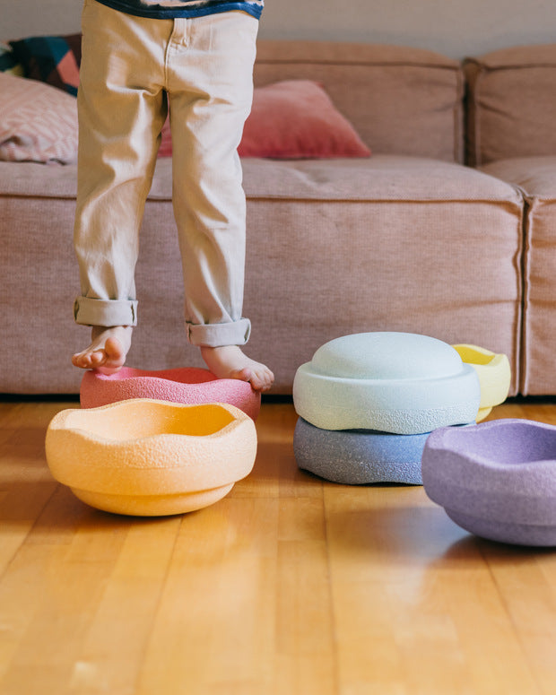 Pastel-colored bean bags on a wooden floor with a child standing nearby.
