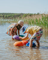 Two children playing with colorful toys in a body of water near reeds.
