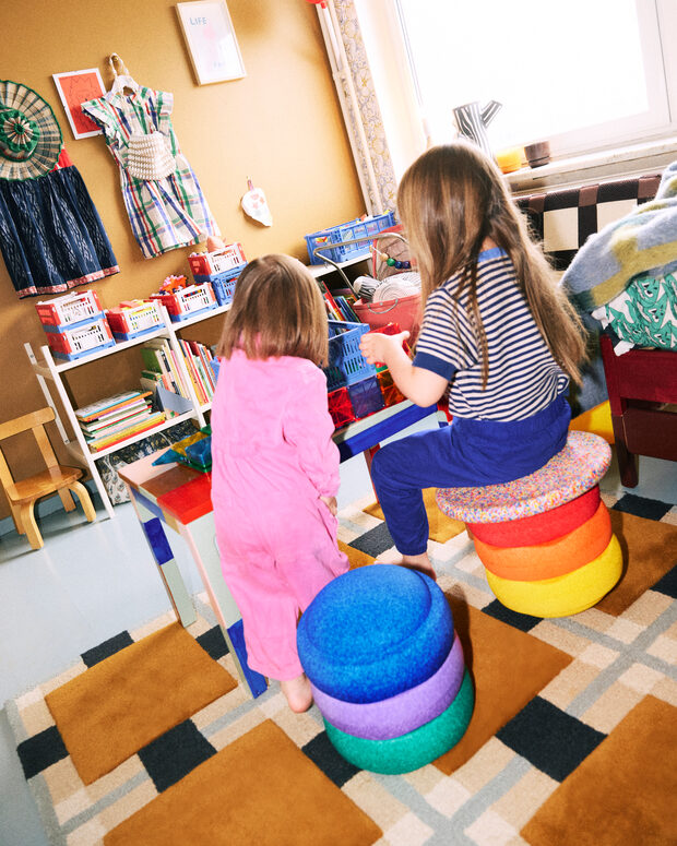 Two children playing with colorful Stapelstein Rainbow Set in a room filled with books and toys.
