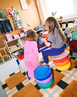 Two children playing with colorful Stapelstein Rainbow Set in a room filled with books and toys.