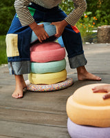 Person sitting on a stack of colorful cushions on a wooden deck.