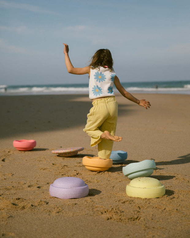 Child playing on a sandy beach with colorful stepping stones