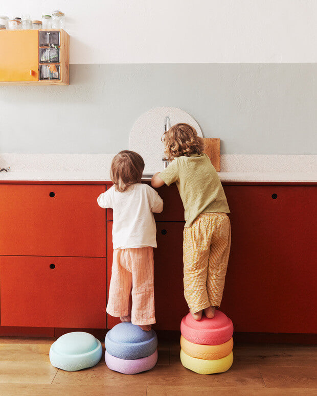 Two children standing on colorful Stapelstein original rainbow pastel in a kitchen.