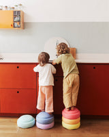 Two children standing on colorful Stapelstein original rainbow pastel in a kitchen.