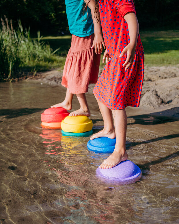 Two children standing on colorful stepping stones in a shallow stream.