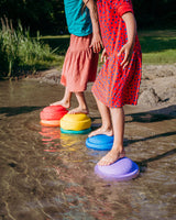 Two children standing on colorful stepping stones in a shallow stream.