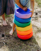 Children playing with a stack of colorful original rainbow outdoors.